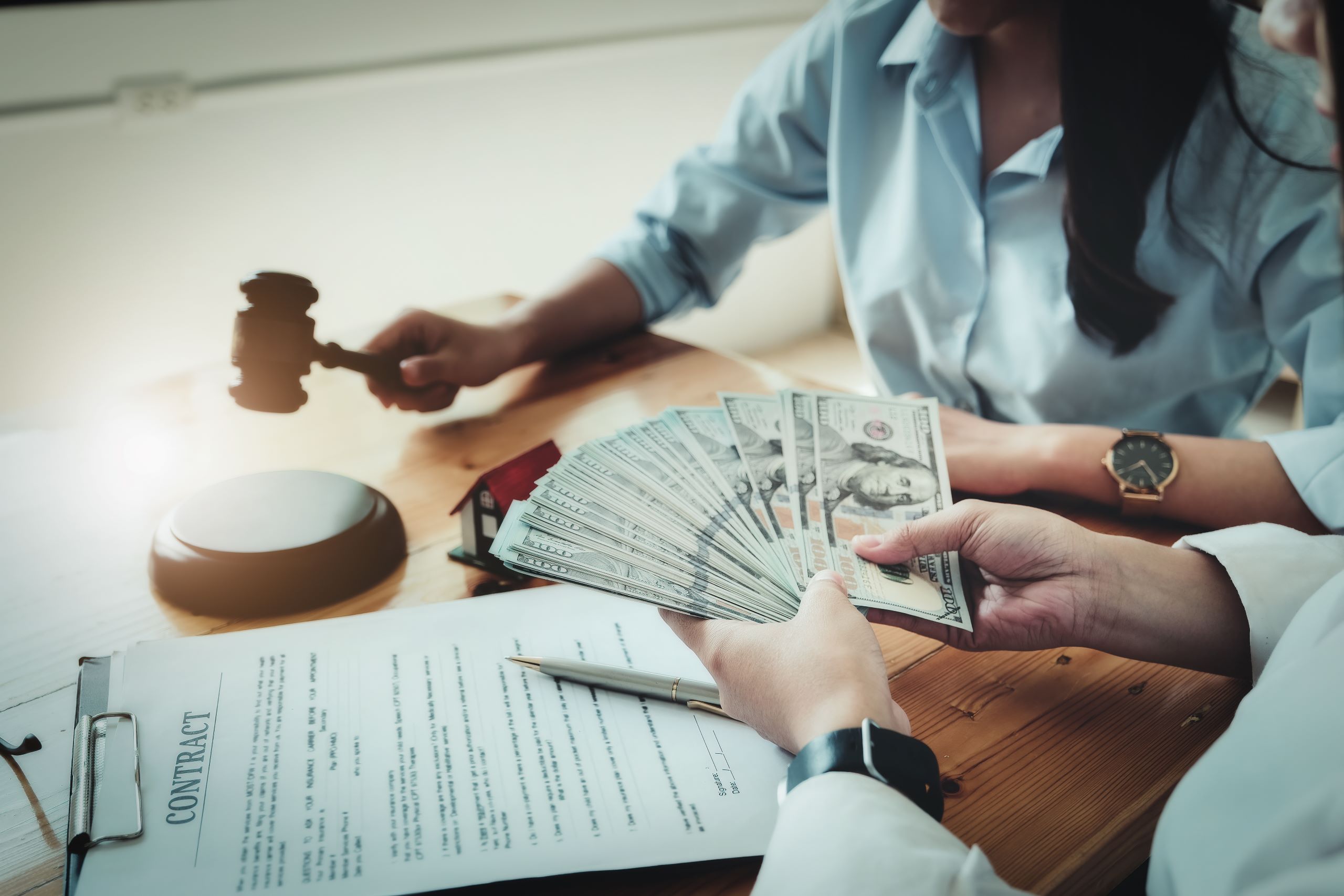 Close-up of a person handing over a stack of cash, with a legal contract, pen, and gavel on the table, symbolizing financial and legal negotiations.
