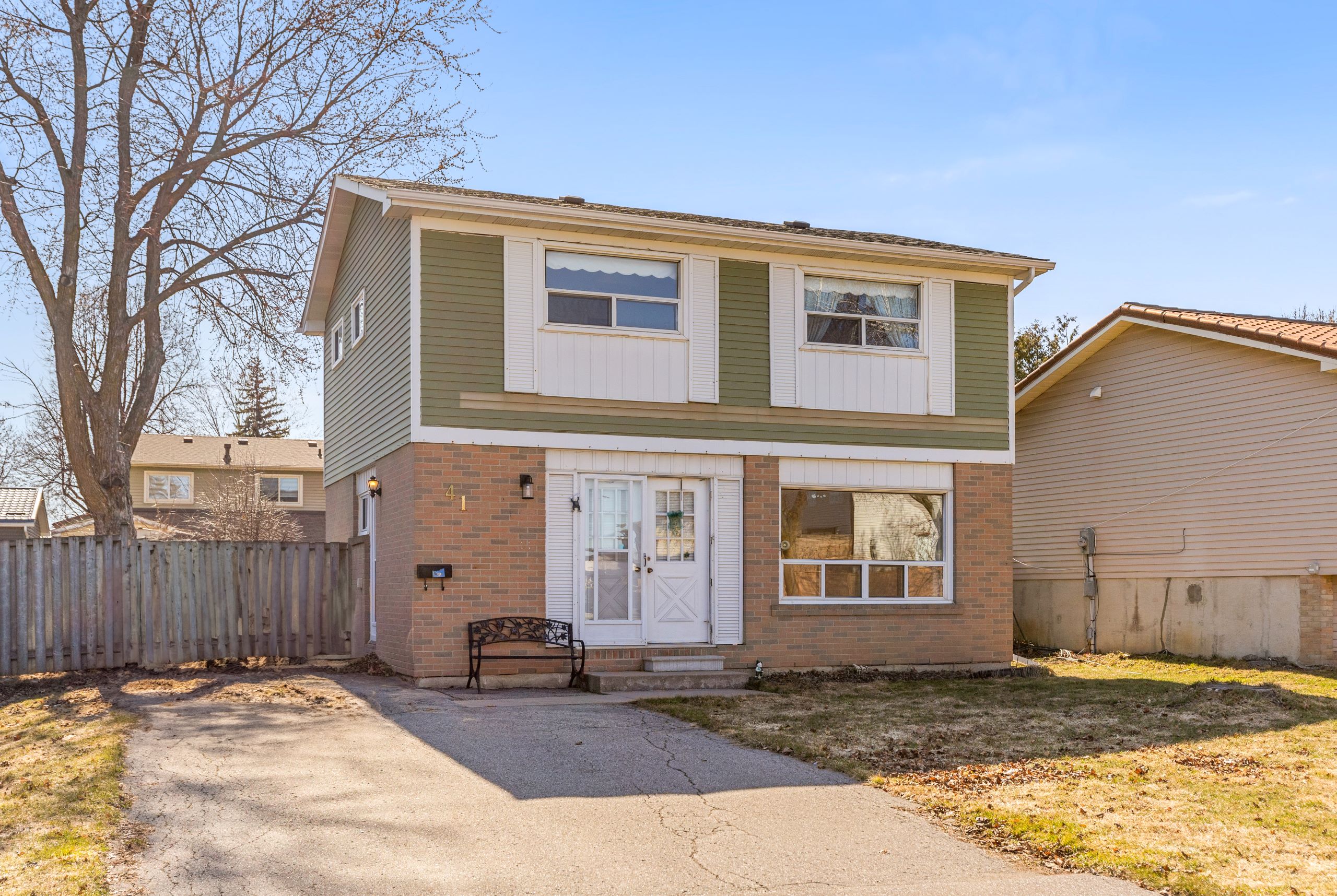 A two-storey detached home located at 41 Carberry Crescent in Brampton, featuring a brick and green siding exterior, a double front door, a large front-facing window, and a private driveway with a bench near the entrance.