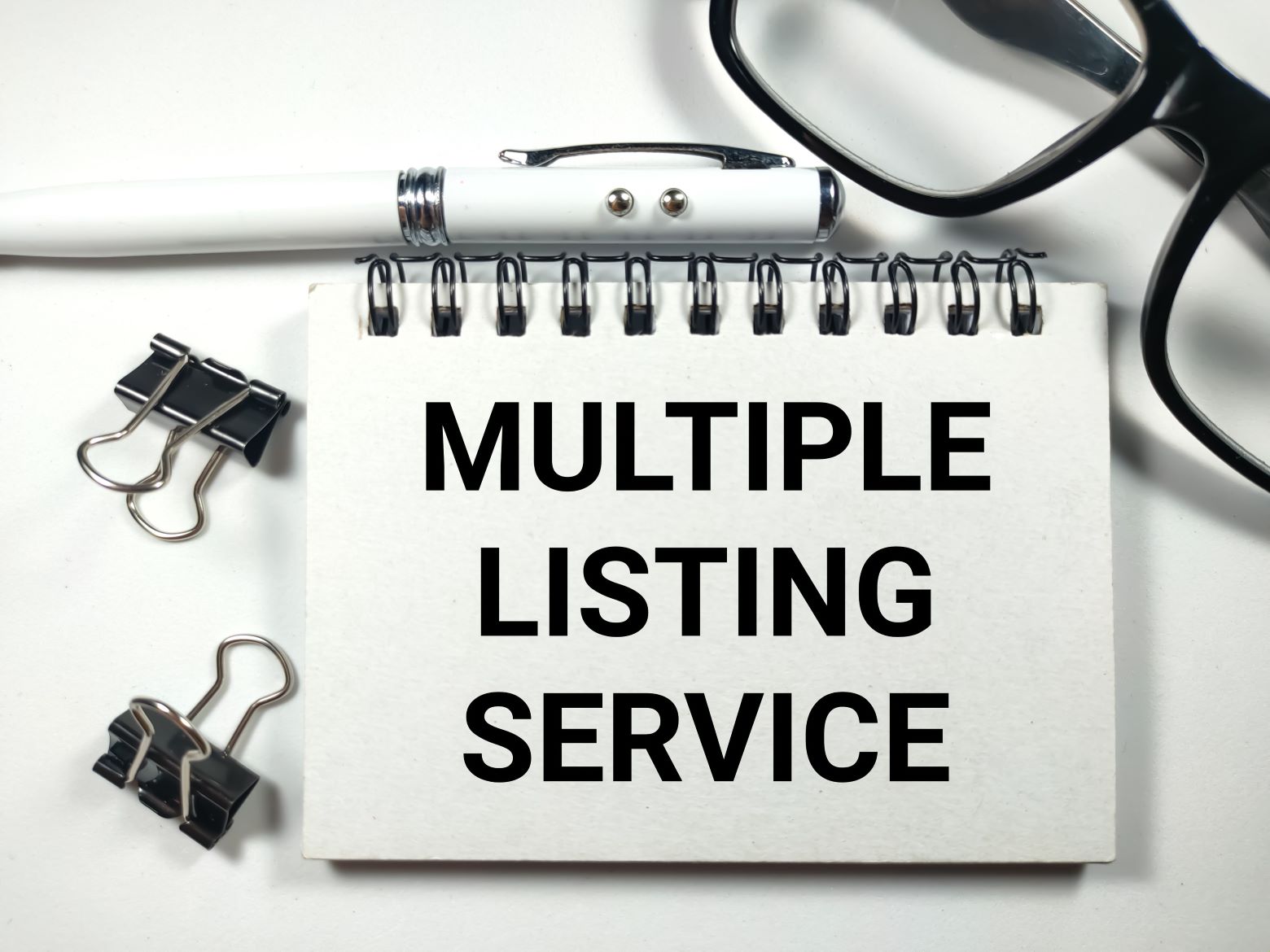 Text MULTIPLE LISTING SERVICE writing on notebook with pen,paper clips and glasses on white background.